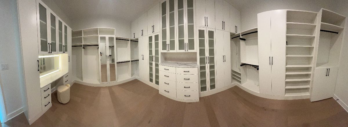 A white walk-in closet with many cabinets, shelves, and hanging rods. The floor is carpeted.