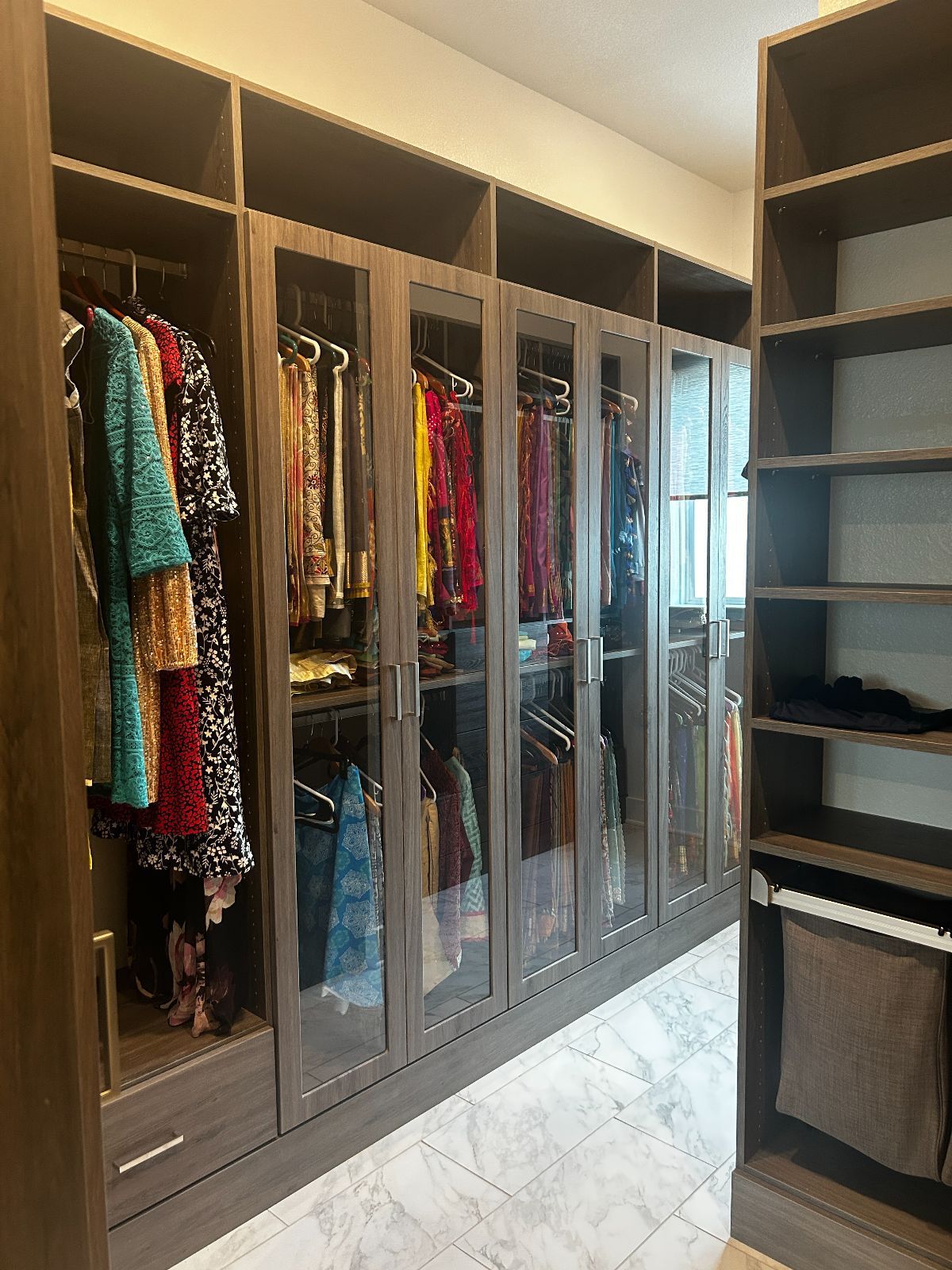 Walk-in closet with dark gray cabinets, glass doors, and clothing hanging inside; open shelves on right.