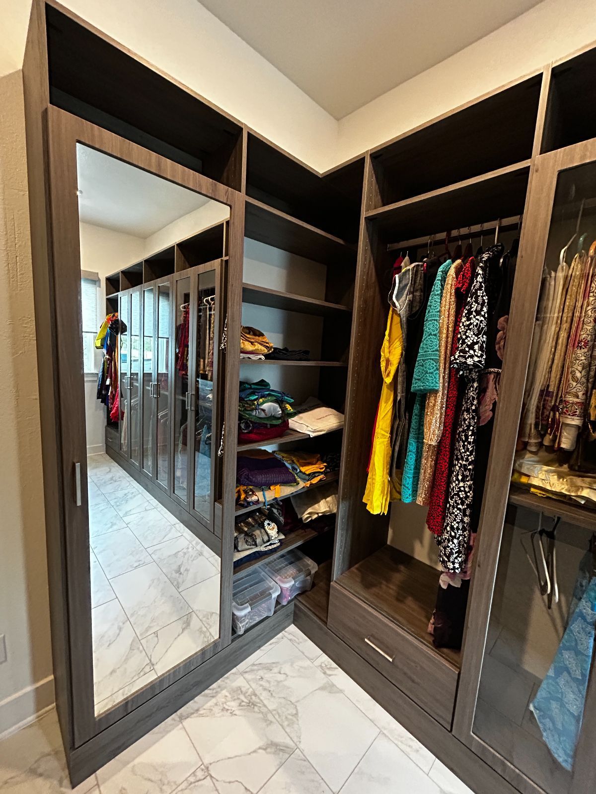 Walk-in closet with dark brown shelving, clothes, and a large mirror reflecting the space.