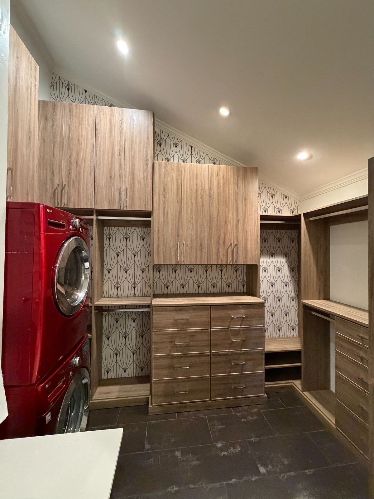 A laundry room with a red washer/dryer set, wooden cabinets, and patterned wallpaper.