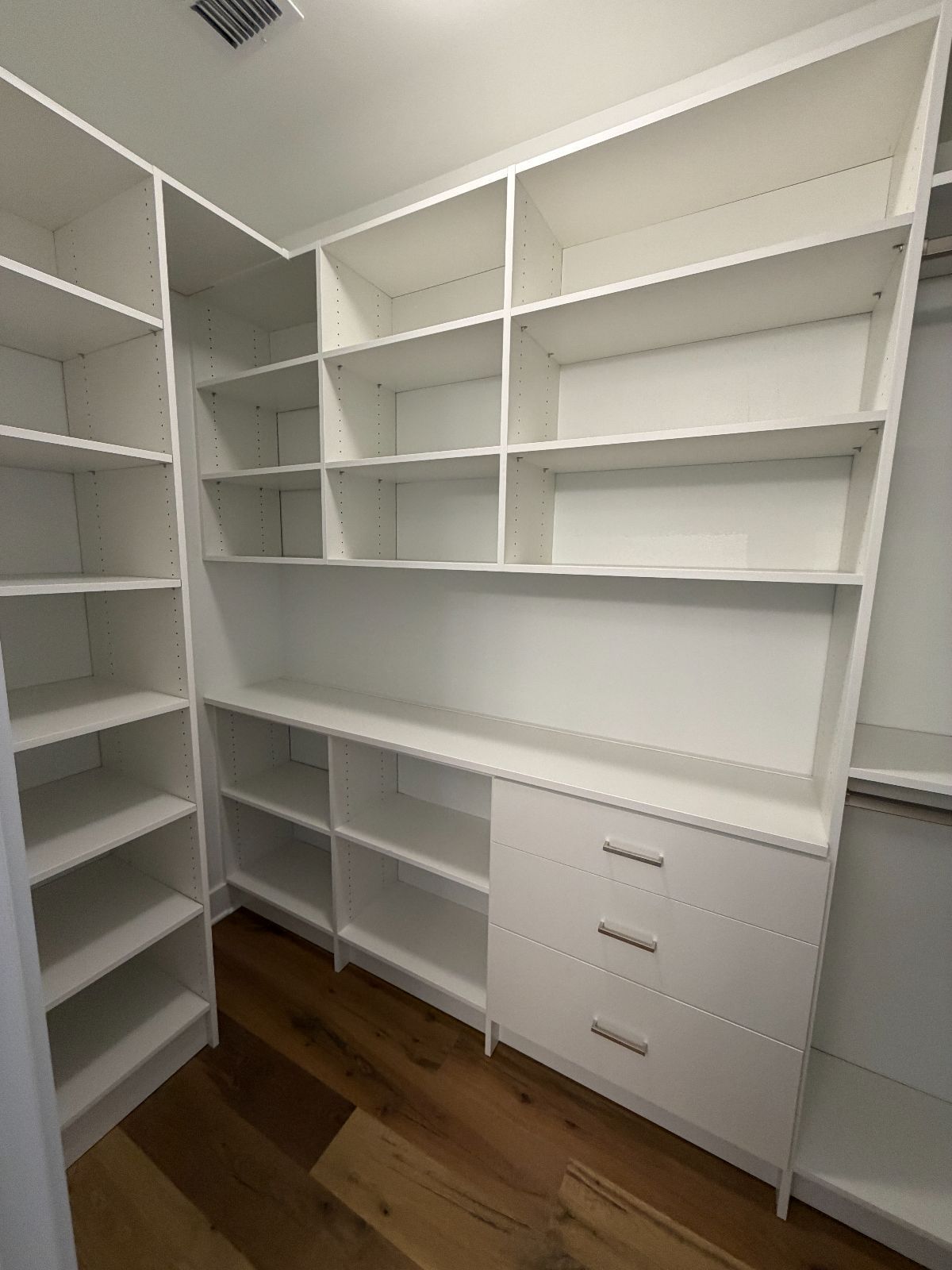 White custom closet with shelves, drawers, and wooden floor.