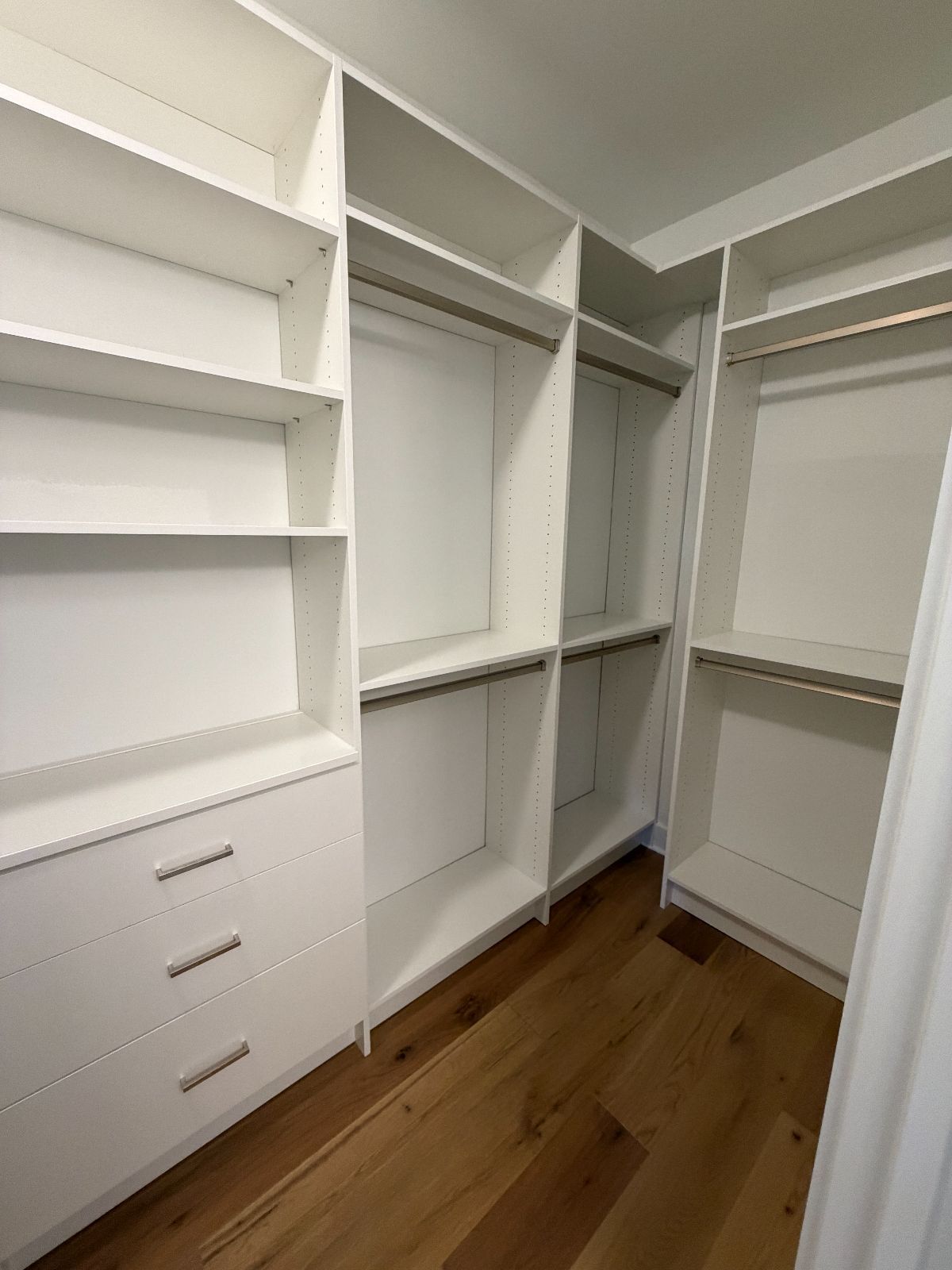 White walk-in closet with shelves, drawers, and hanging rods. Hardwood floor.