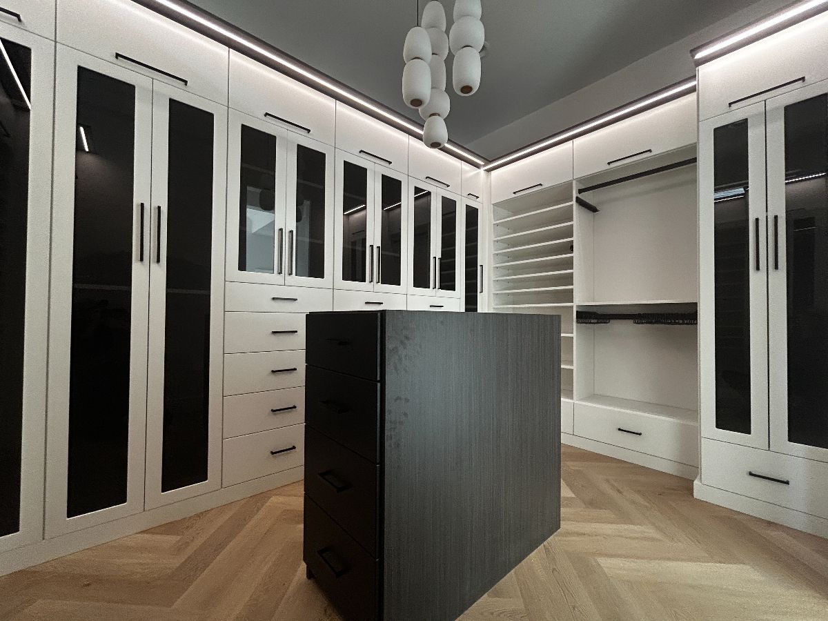Walk-in closet with white cabinets, dark glass doors, and a dark wooden center island.