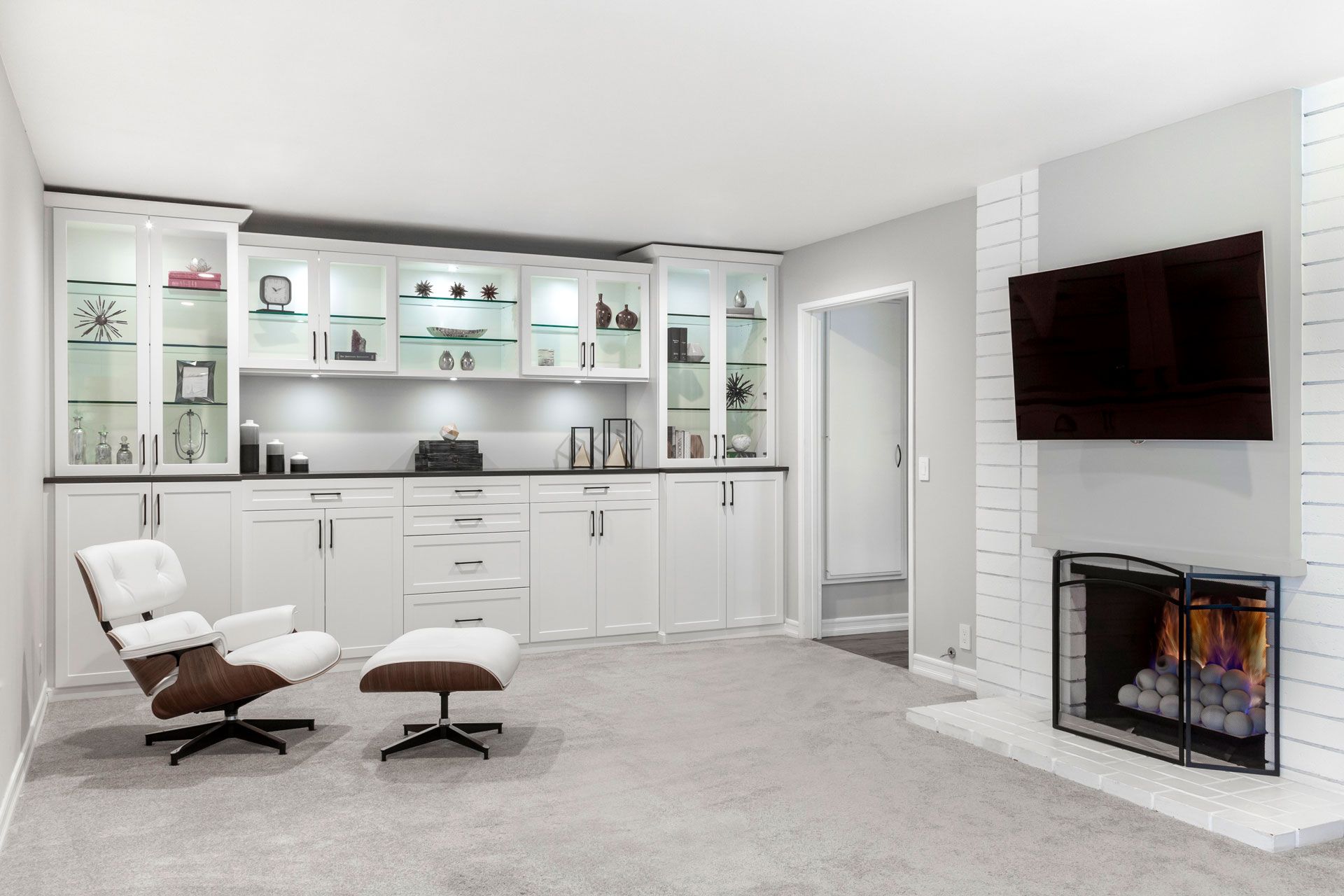 a living room with a fireplace , entertainment center, chair , ottoman and television .