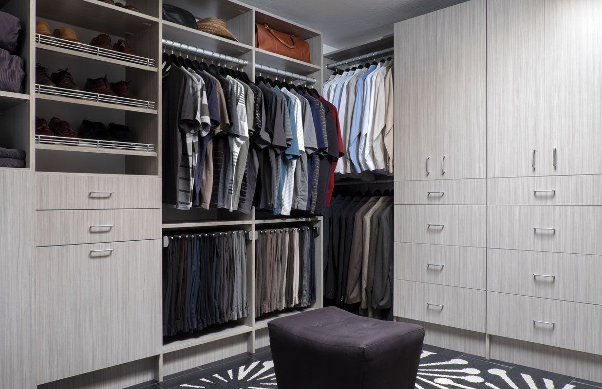 a walk in closet filled with lots of clothes and a black ottoman .