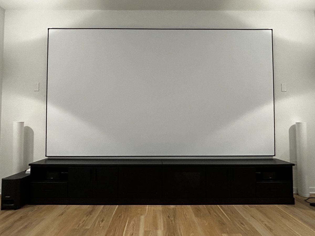 Large white projection screen on black media console, flanked by speakers, in a room with sconces.