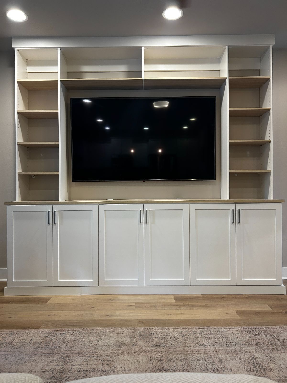 Built-in white media center with TV, shelves, and cabinets against a gray wall.