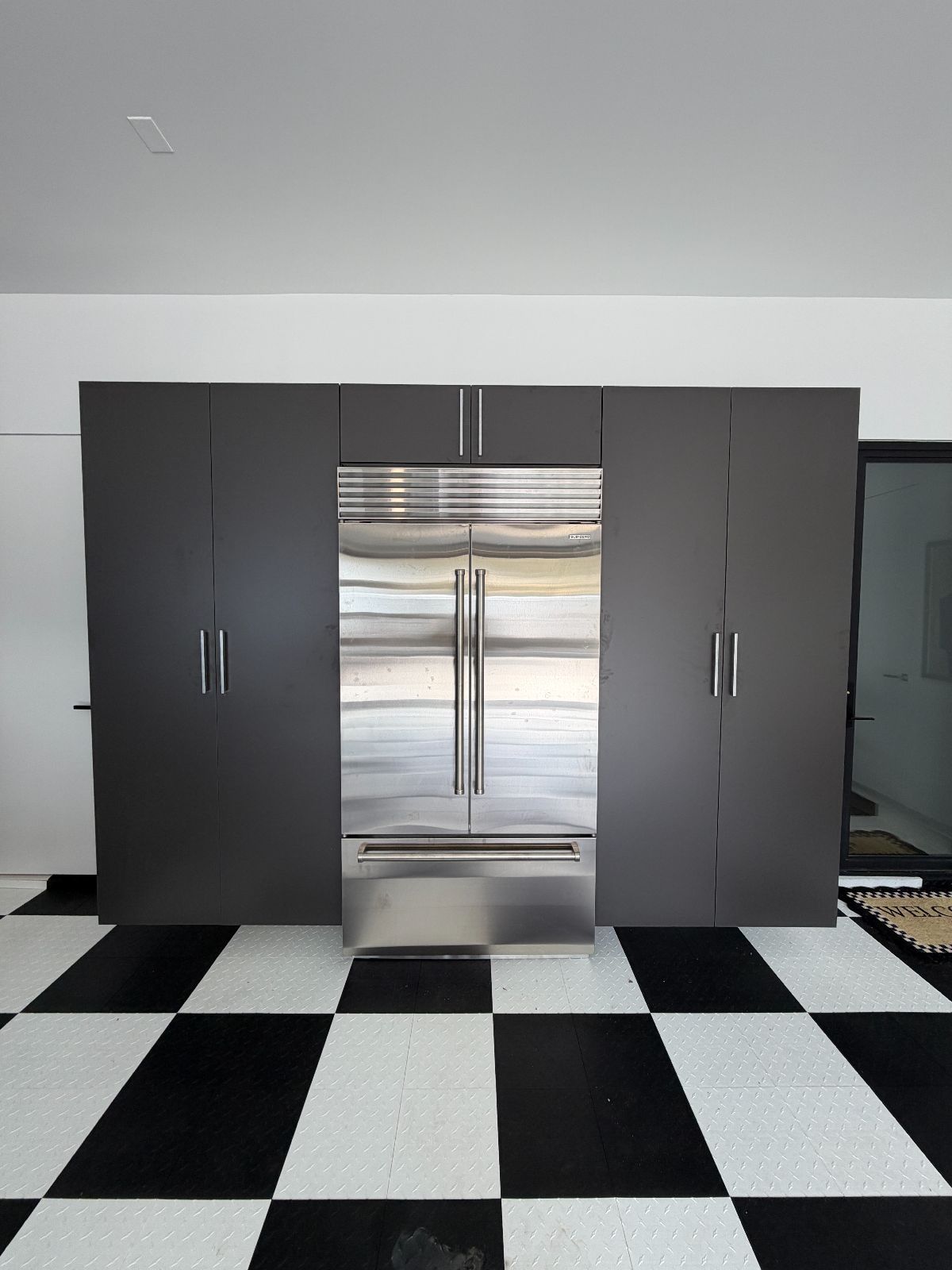 Stainless steel refrigerator flanked by dark gray cabinets, on a checkered floor.