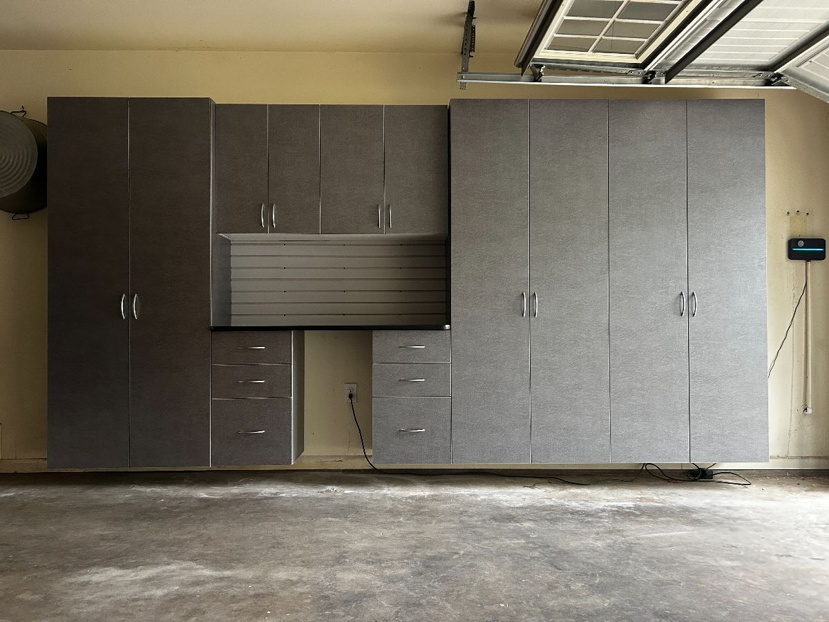 Garage storage cabinets, gray color, with drawers and tall doors, mounted on a light beige wall.