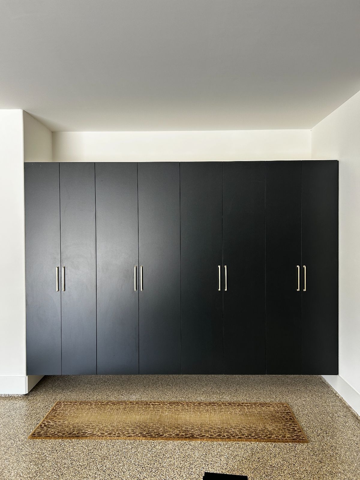 Black built-in closet with six doors and silver handles against a white wall. Tan rug on speckled floor.
