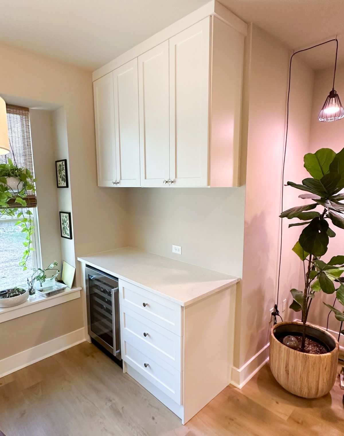 A kitchen with white cabinets , a refrigerator , and a potted plant.
