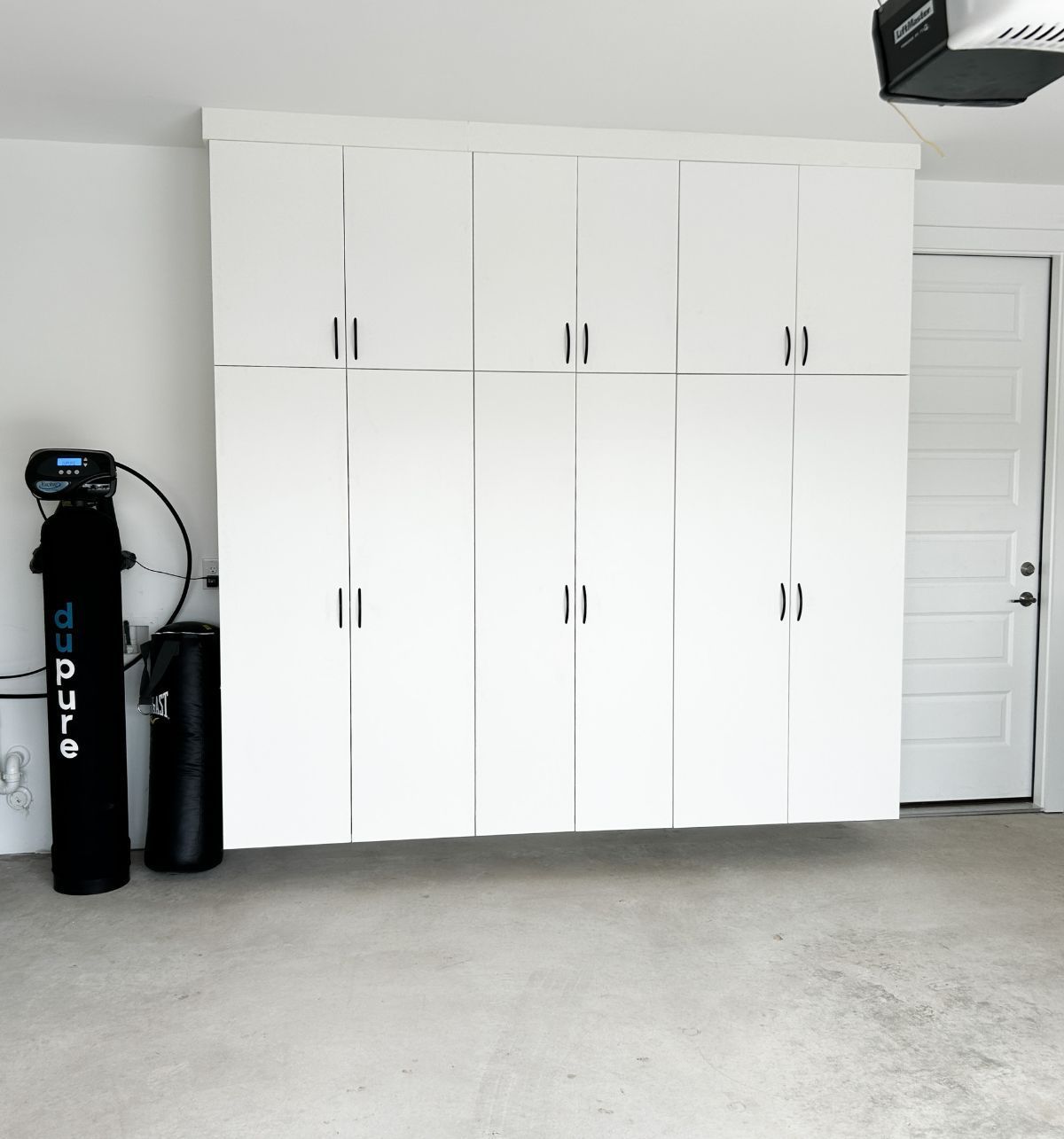A garage with lots of white cabinets and a black cylinder that says o.t.c.u.