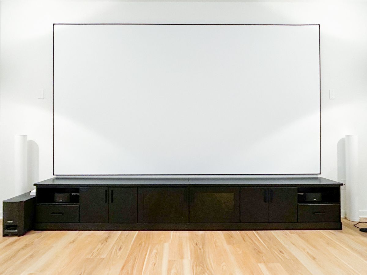 an entertainment room with white screen and custom cabinet system below