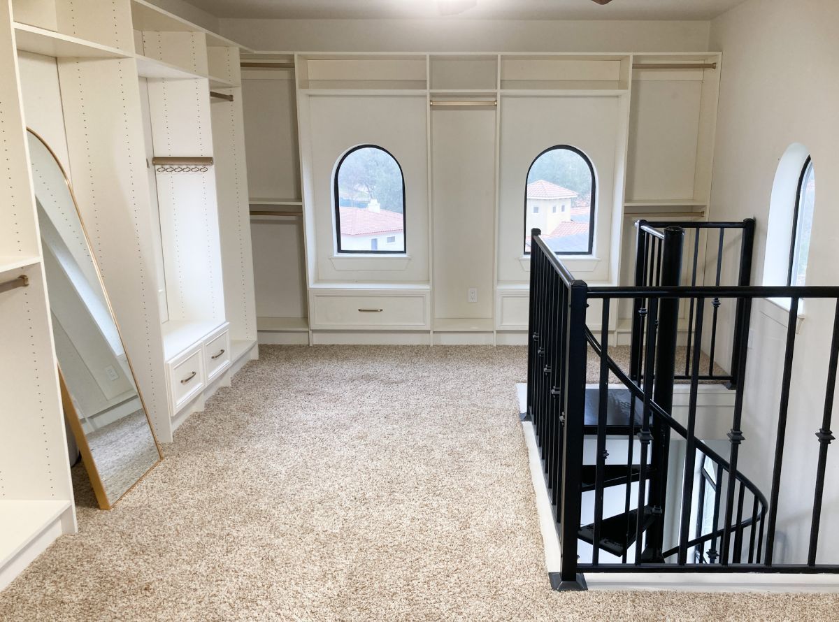 An empty walk in closet with a spiral staircase and a mirror.