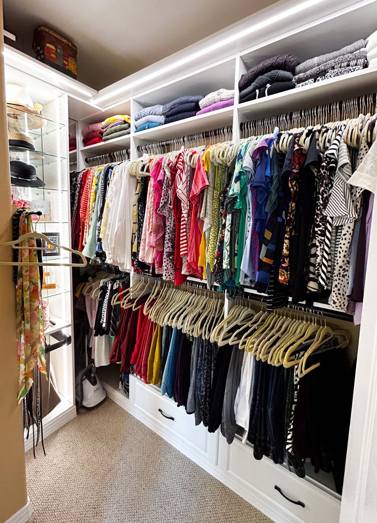 A walk in closet filled with lots of clothes and a vacuum cleaner.