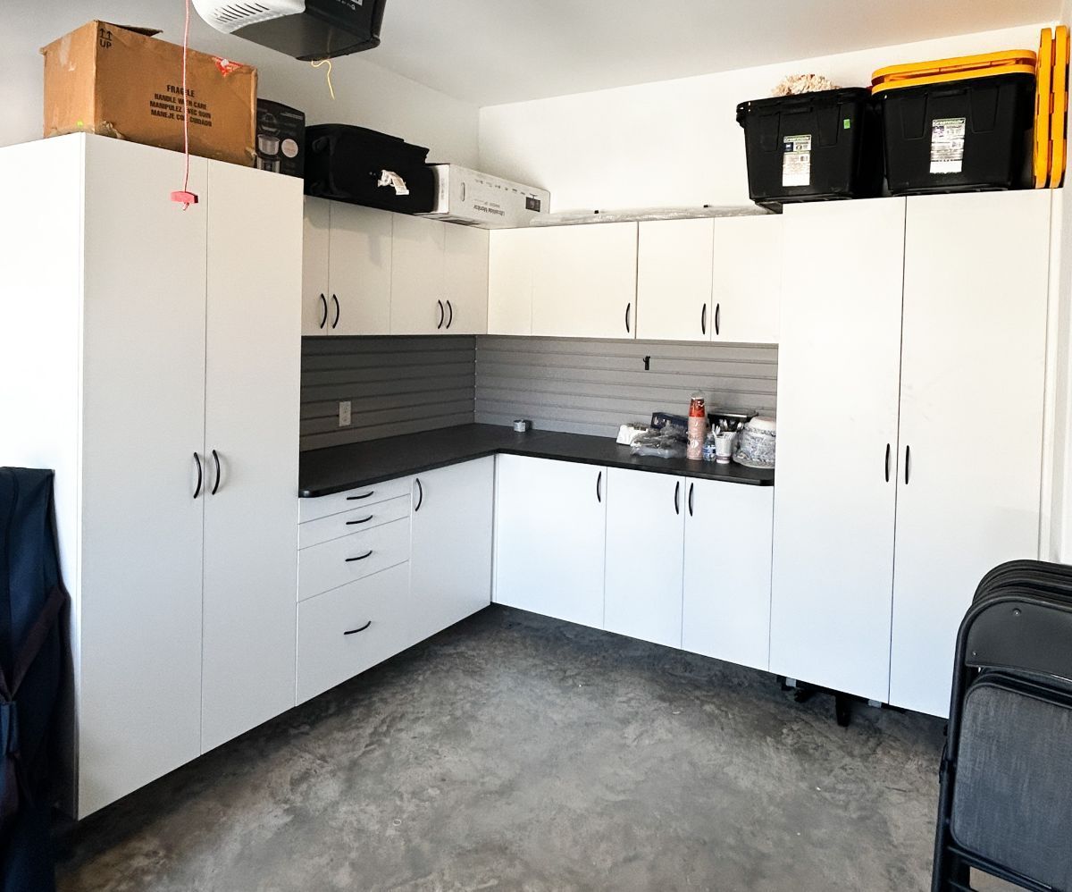 A kitchen with white cabinets and black counter tops in a garage.