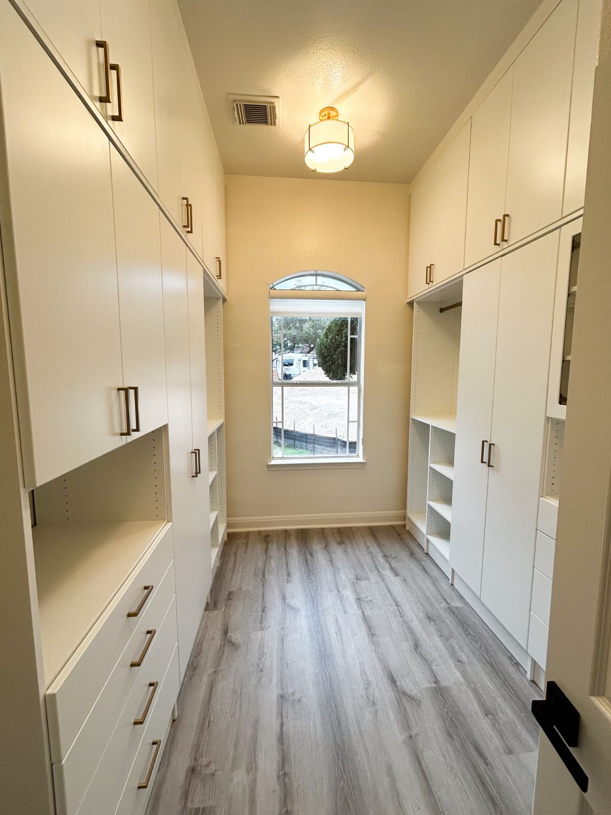 A long hallway with white cabinets and drawers and a window.