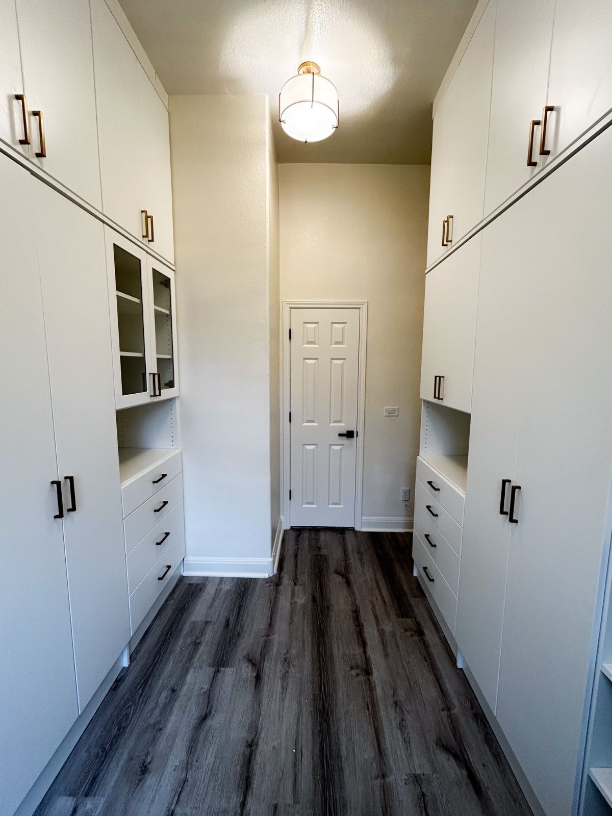 A long hallway with white cabinets and wooden floors leading to a door.