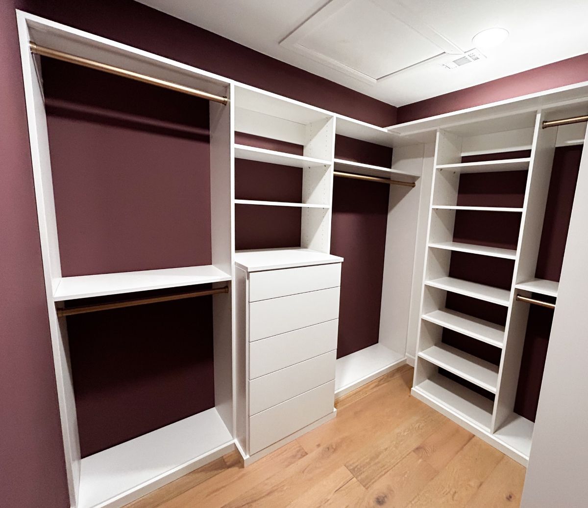 A walk in closet with purple walls and white shelves.