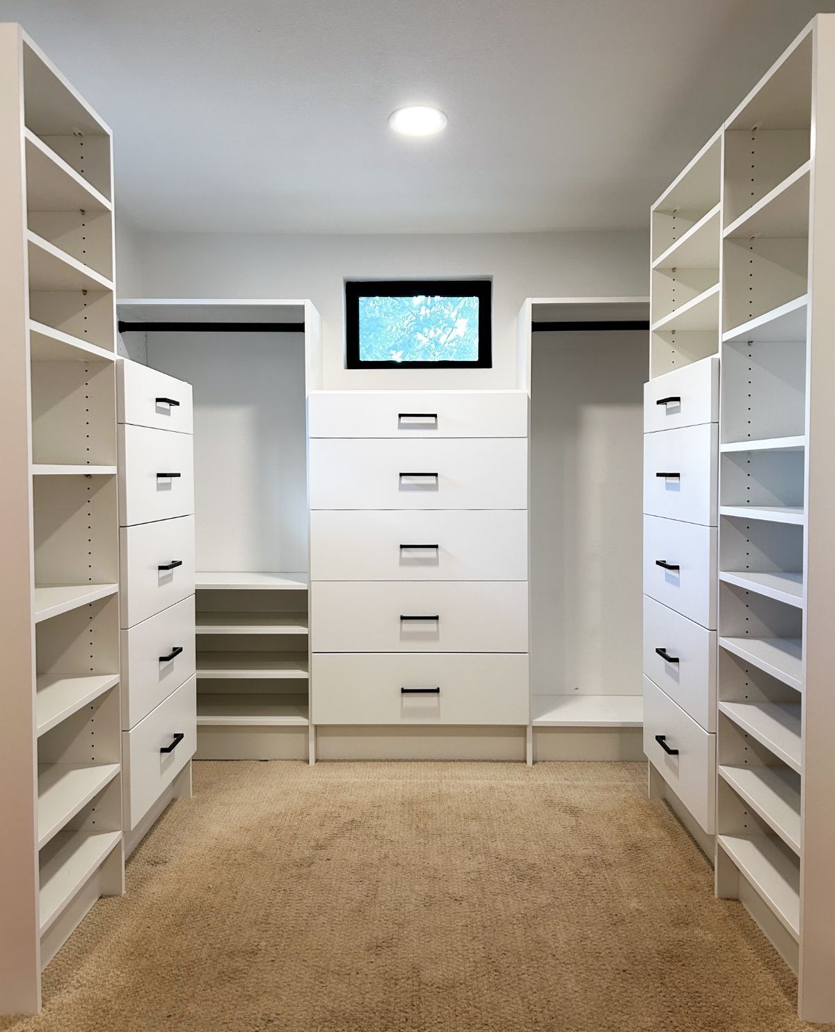 A walk in closet with lots of shelves and drawers and a window.