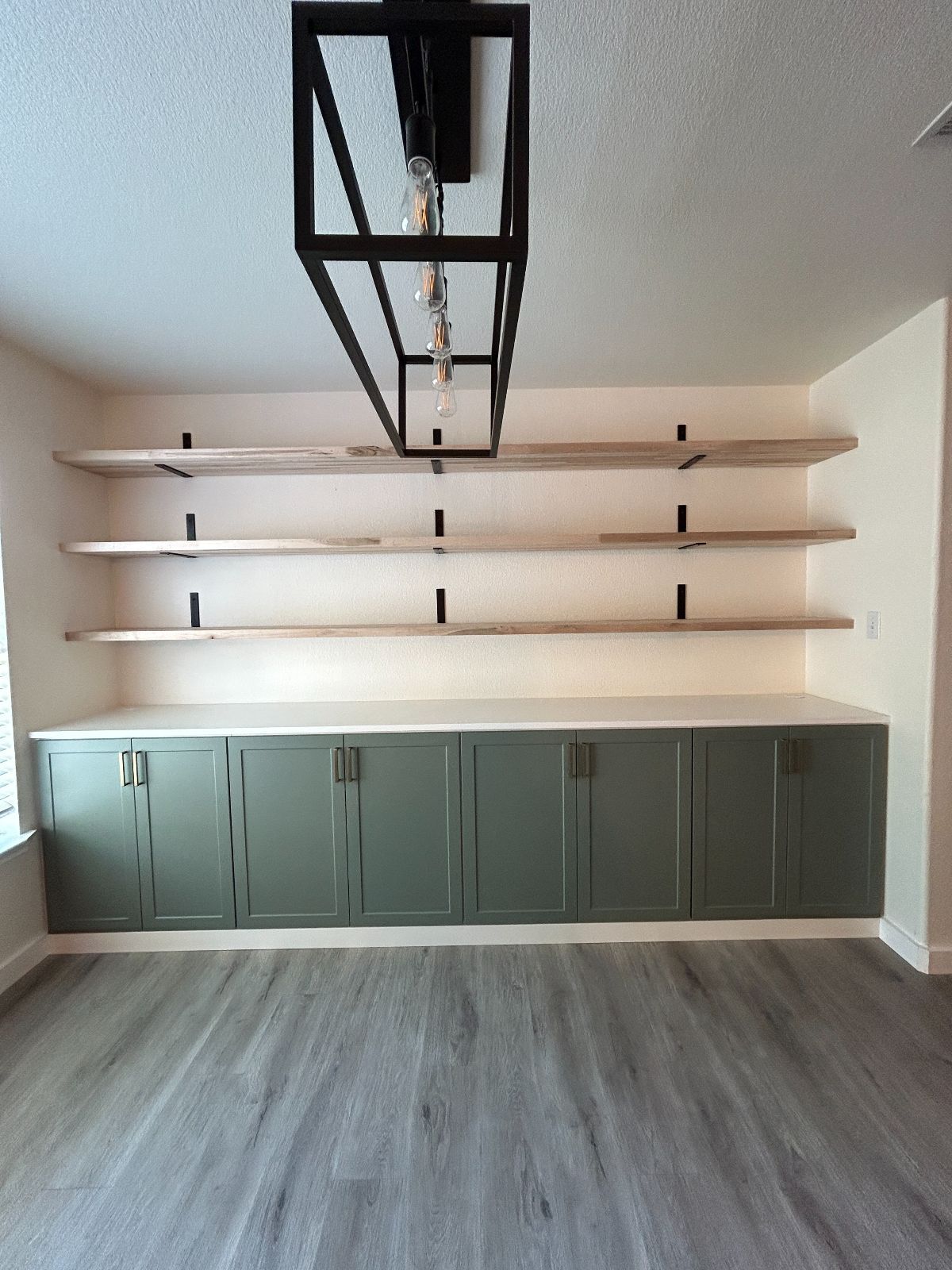Built-in storage with green cabinets, open shelves, and a rectangular light fixture. Light wood and gray floors.