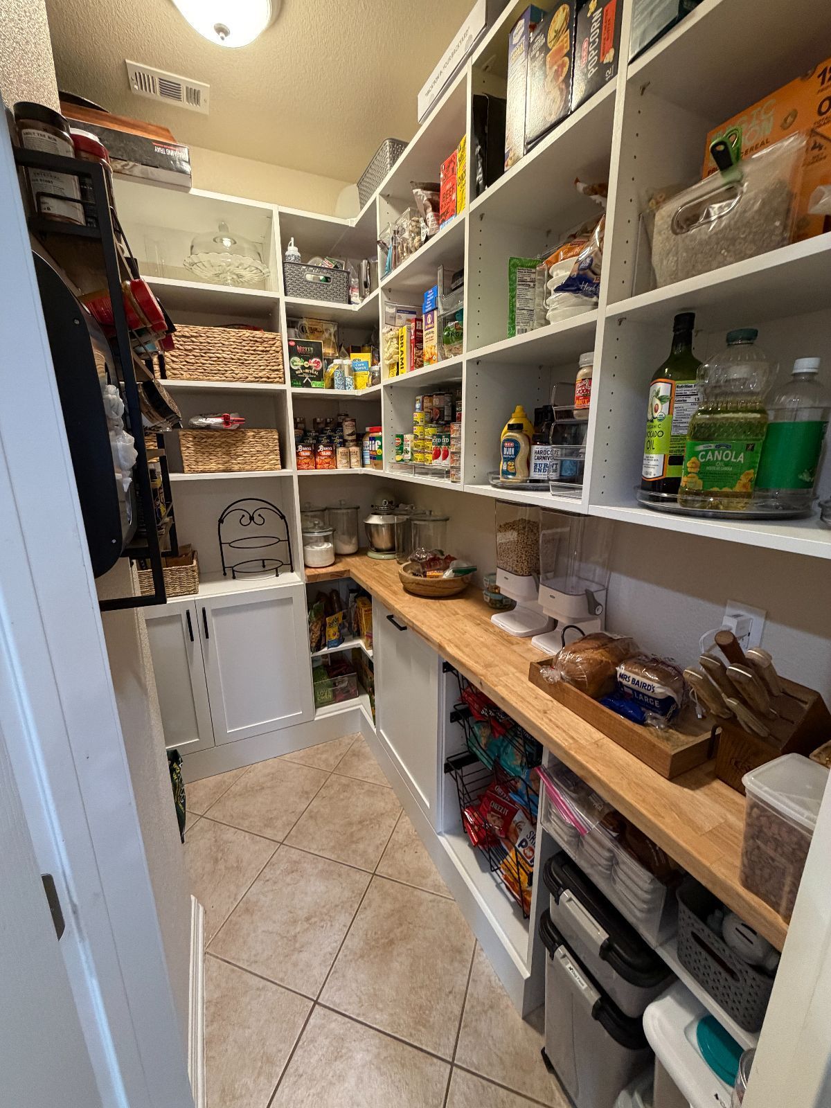 Walk-in pantry with white shelves filled with food items and wooden countertops.