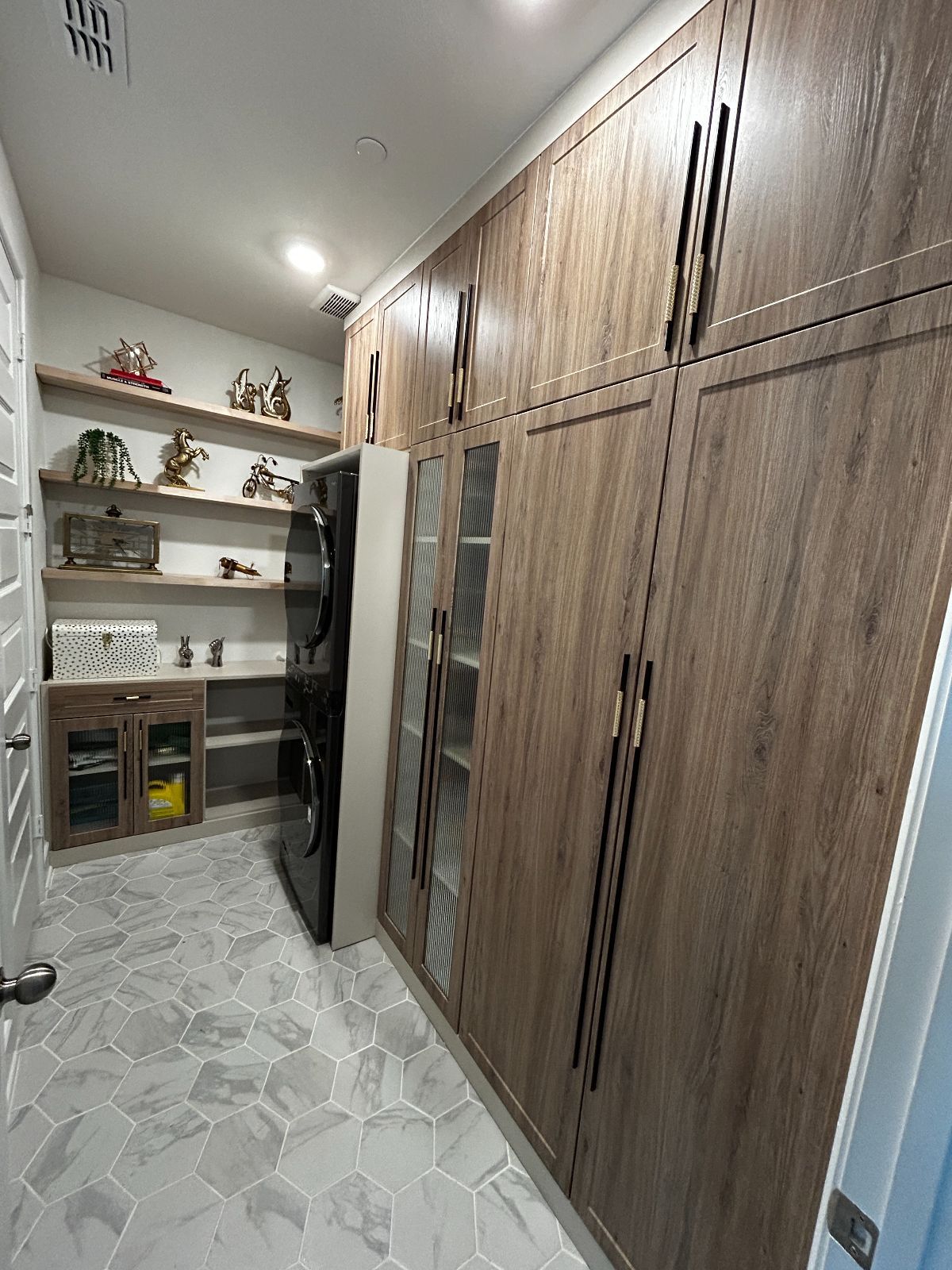 Closet with wooden cabinets and shelves displaying decorative items; gray tiled floor.