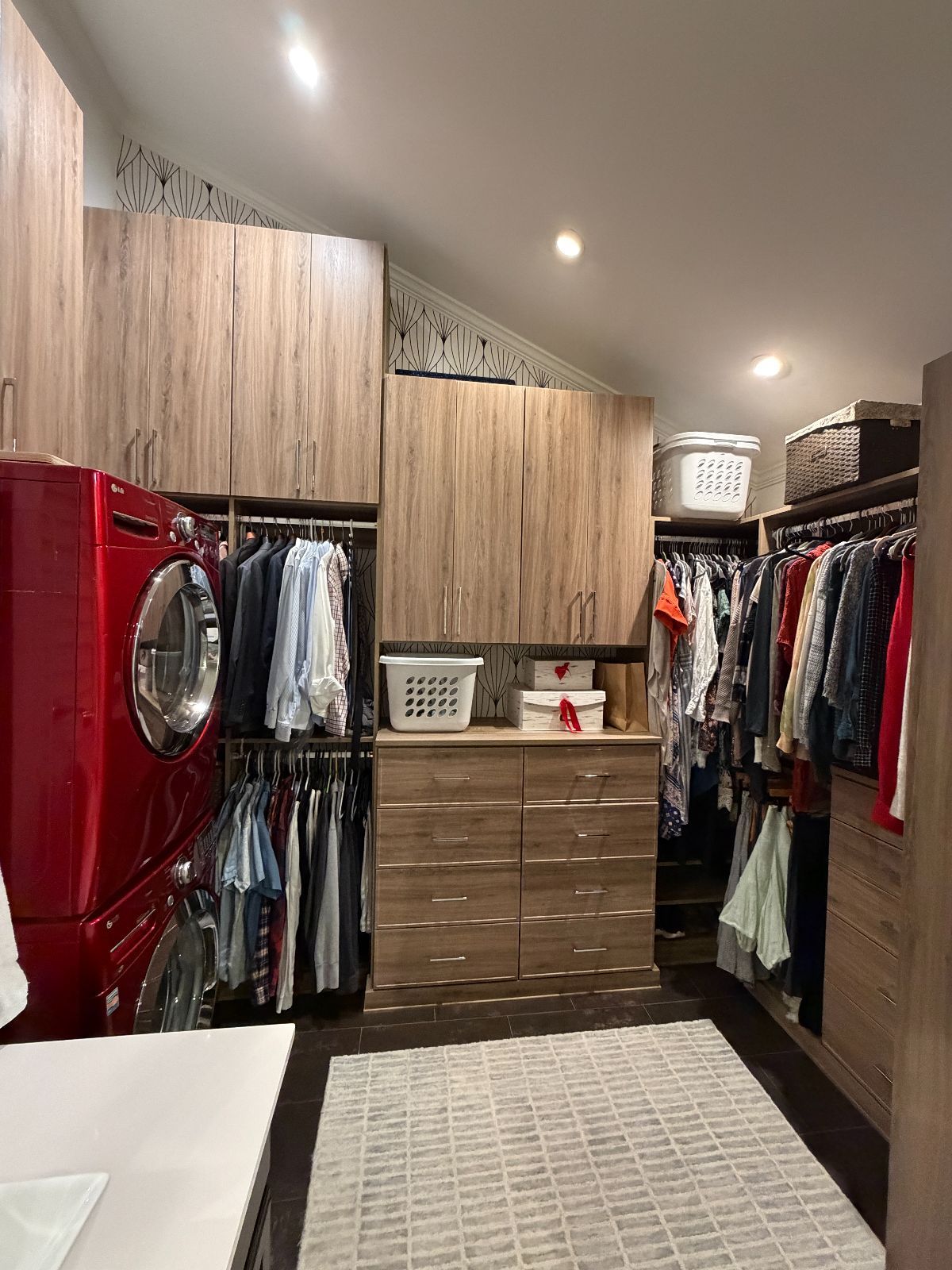 Walk-in closet with brown cabinets, a red washer, hanging clothes, and a beige rug.