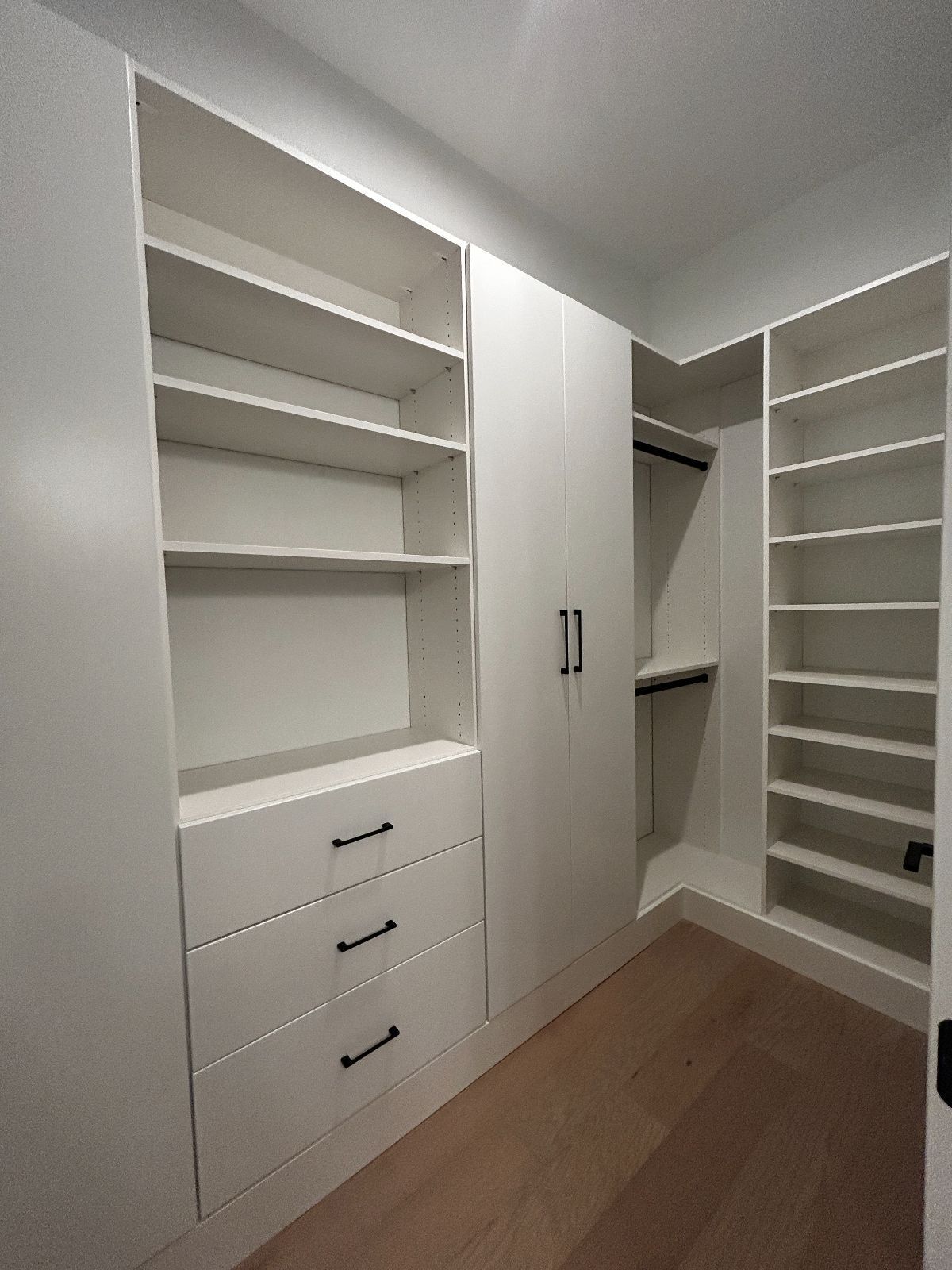 White custom closet with shelves, drawers, and hanging rod. Beige floor, white walls.
