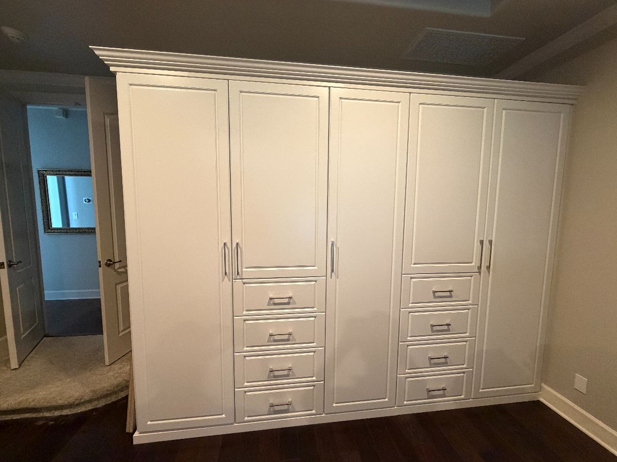 White built-in closet with drawers and cabinets in a bedroom. Dark wood floor.