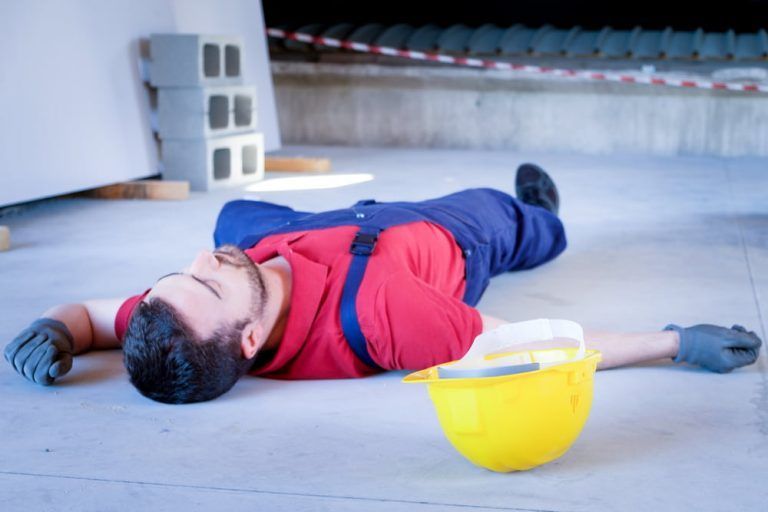 A construction worker is laying on the ground next to a hard hat.