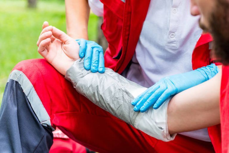 A person with a bandage on their arm is being helped by a paramedic.