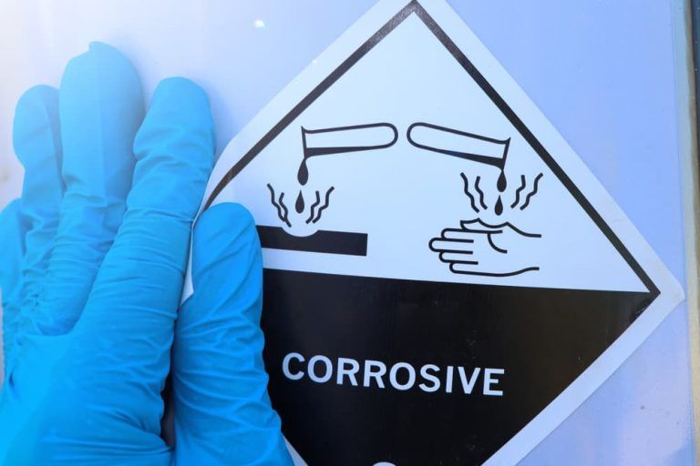 A person wearing blue gloves is holding a sign that says corrosive