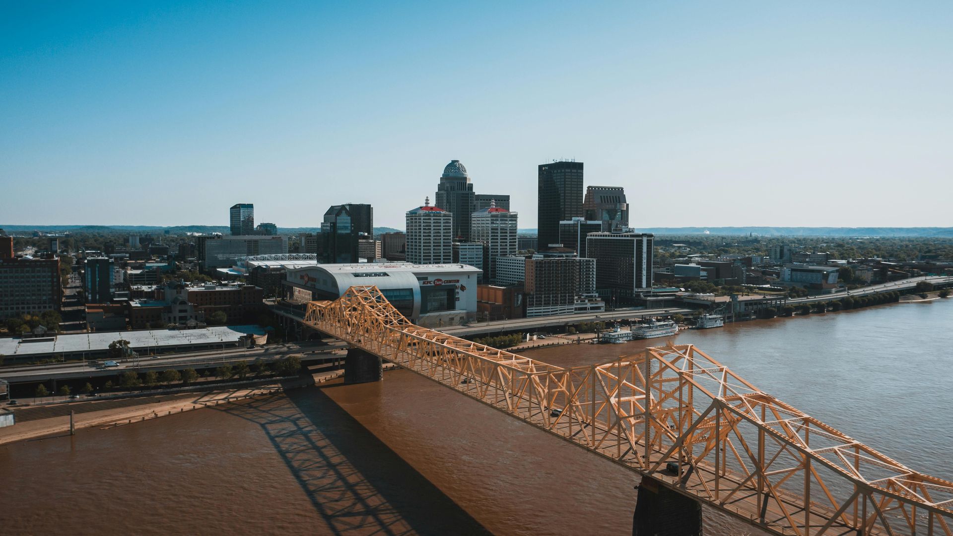 An aerial view of a bridge over a river with a city in the background.