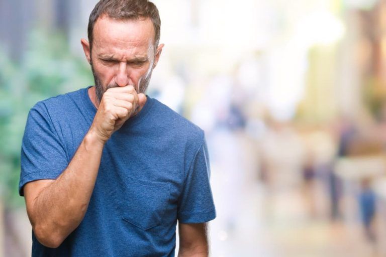 A man is coughing while wearing a blue shirt.