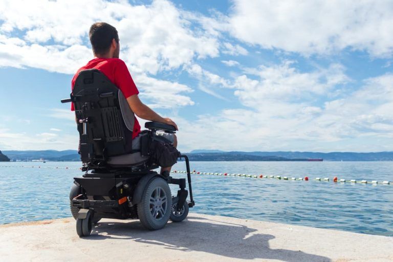 A man in a wheelchair is sitting on a pier looking at the ocean.