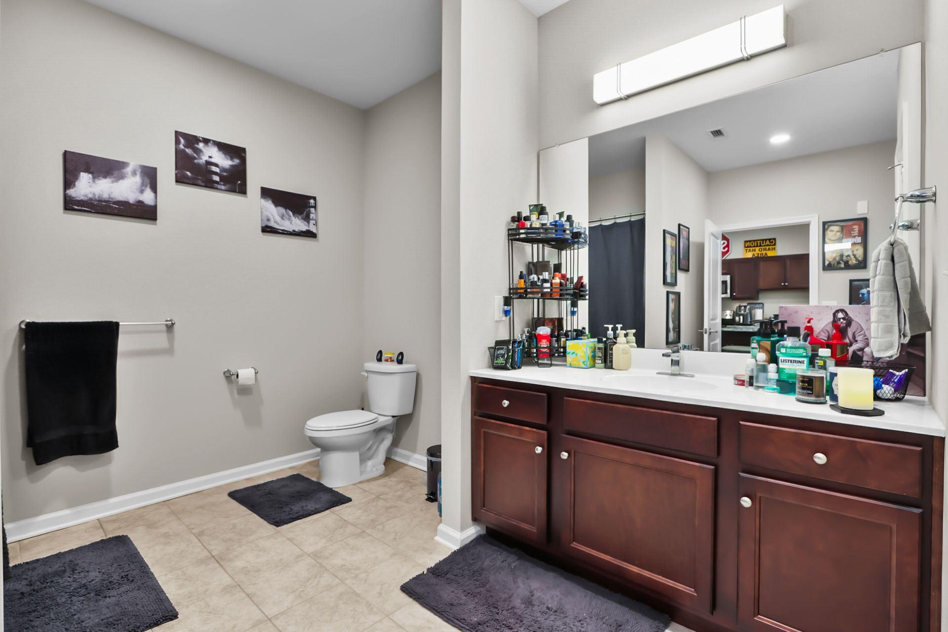 Bathroom with tan tile floor, dark brown vanity, and framed art.