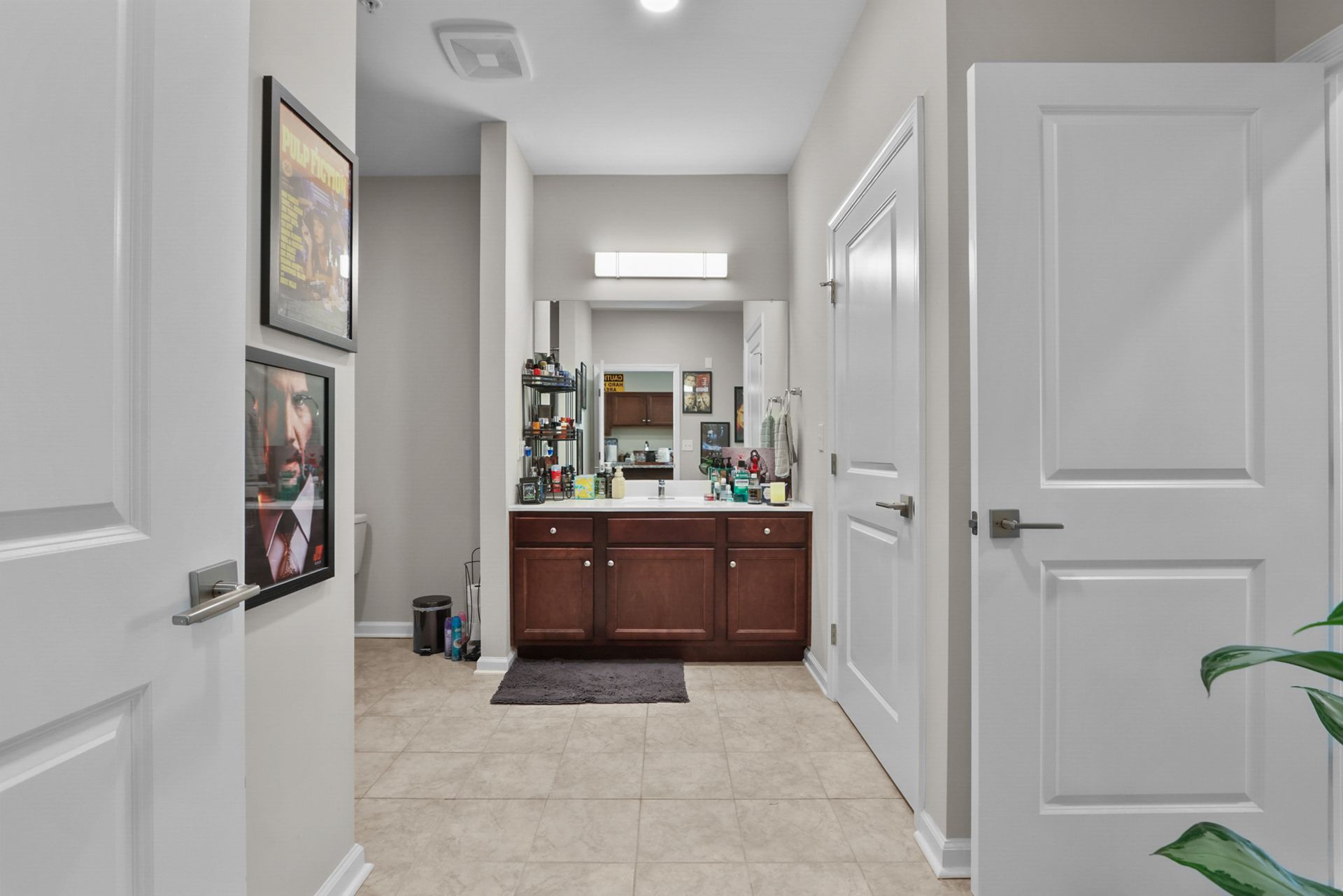Hallway leading to a bathroom. White doors on both sides. Brown vanity, mirror, and toiletries visible.