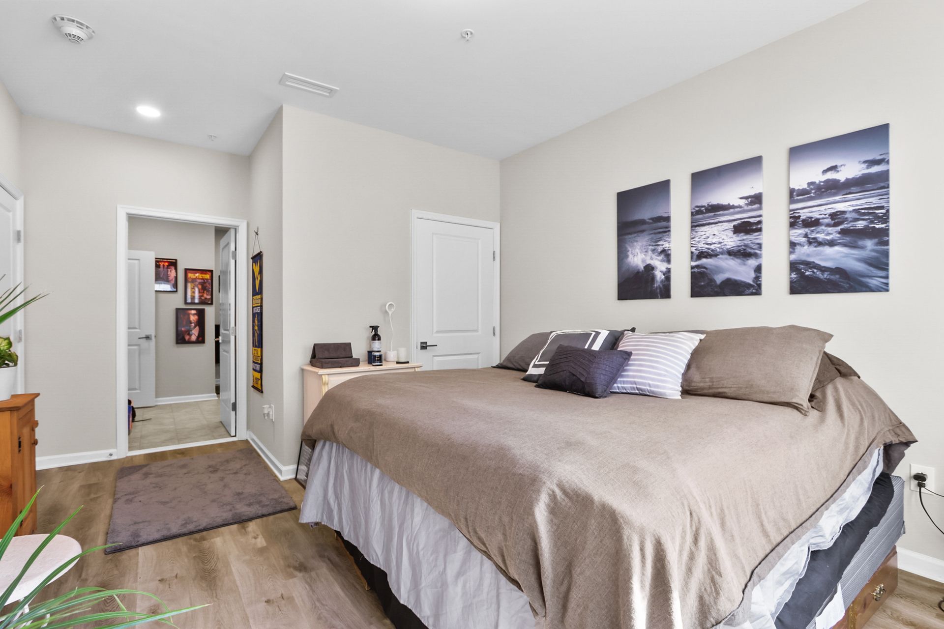 Bedroom with a bed, artwork, doorway to a hallway with pictures on the wall, and wood-look flooring.