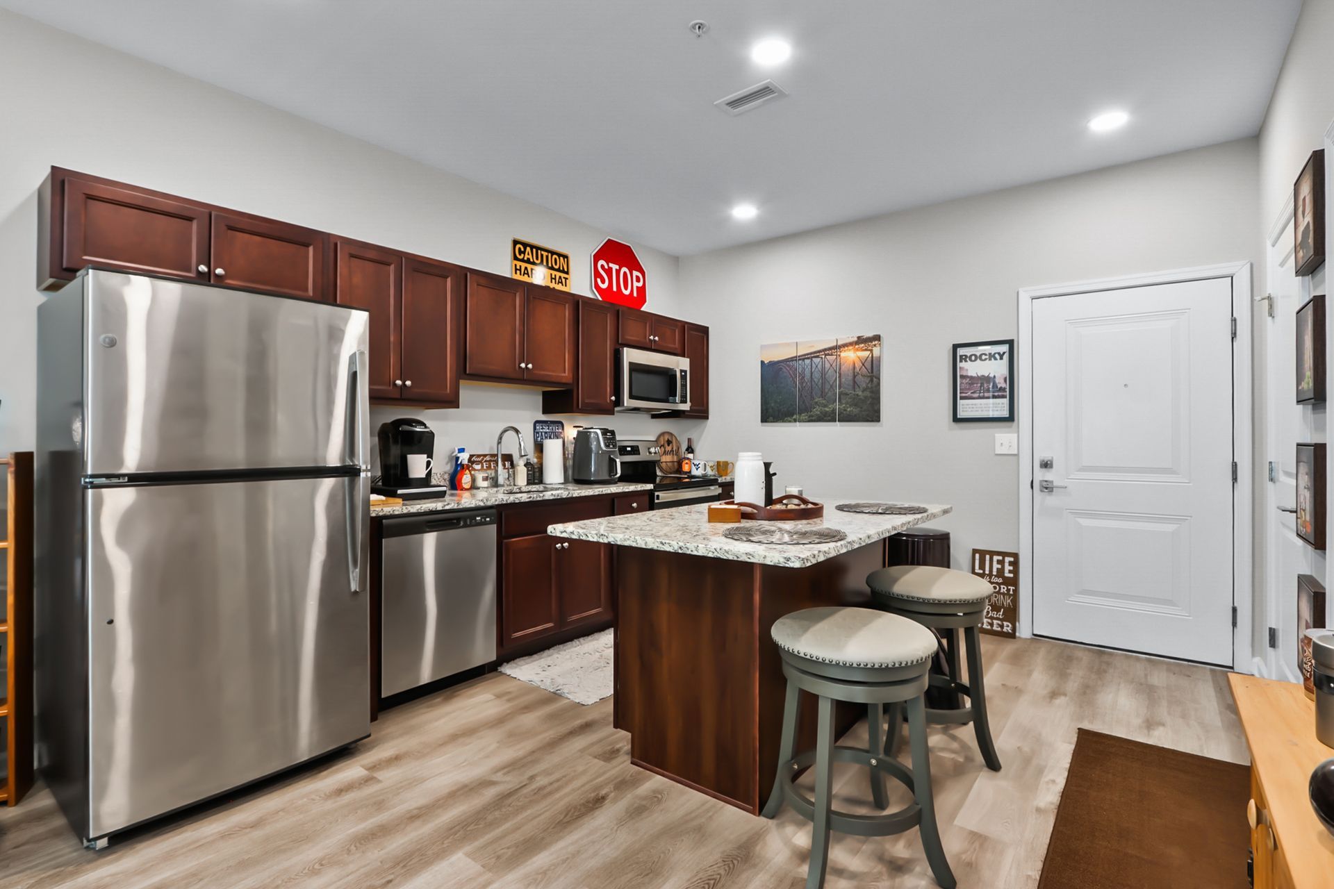 Modern kitchen with stainless steel appliances, brown cabinets, and a granite island with two stools.