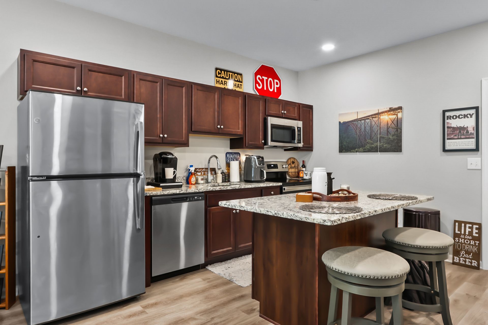 Stainless steel kitchen with dark cabinets, island with stools, and appliances.