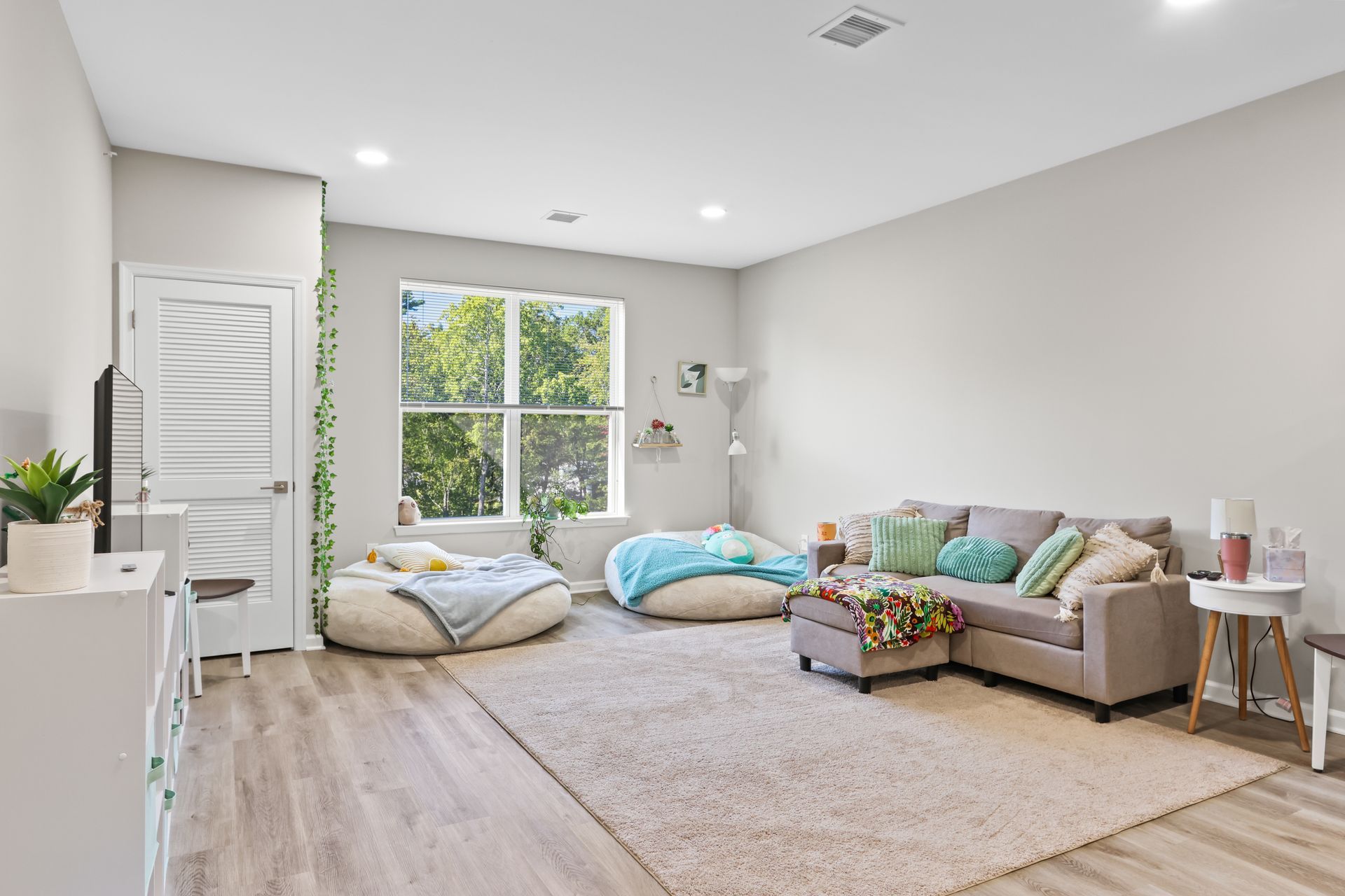 Spacious living room with gray sofa, bean bags, and large window overlooking trees.