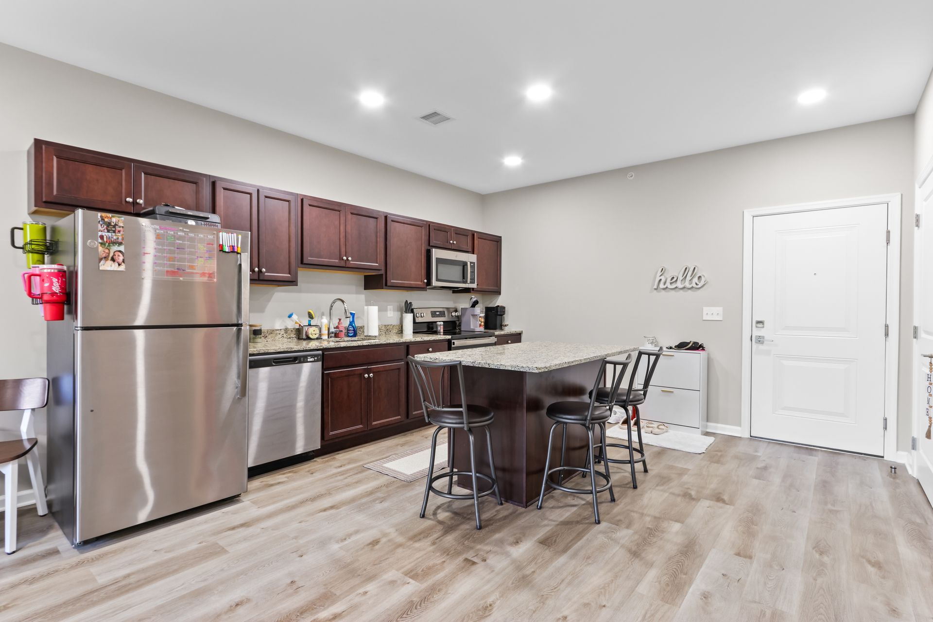 A kitchen with stainless steel appliances, dark cabinets, a kitchen island, and a white door.