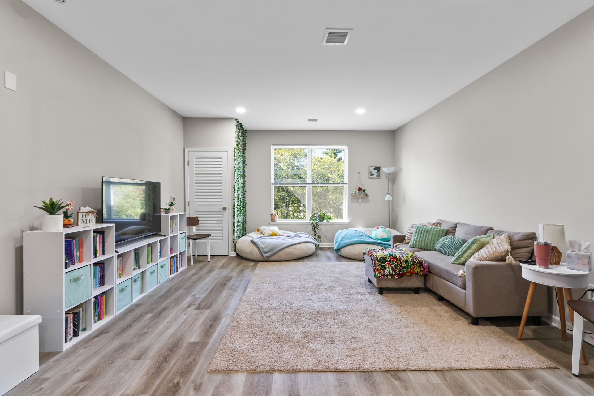 Spacious living room with gray walls, sectional sofa, bean bags, rug, and bookshelves.