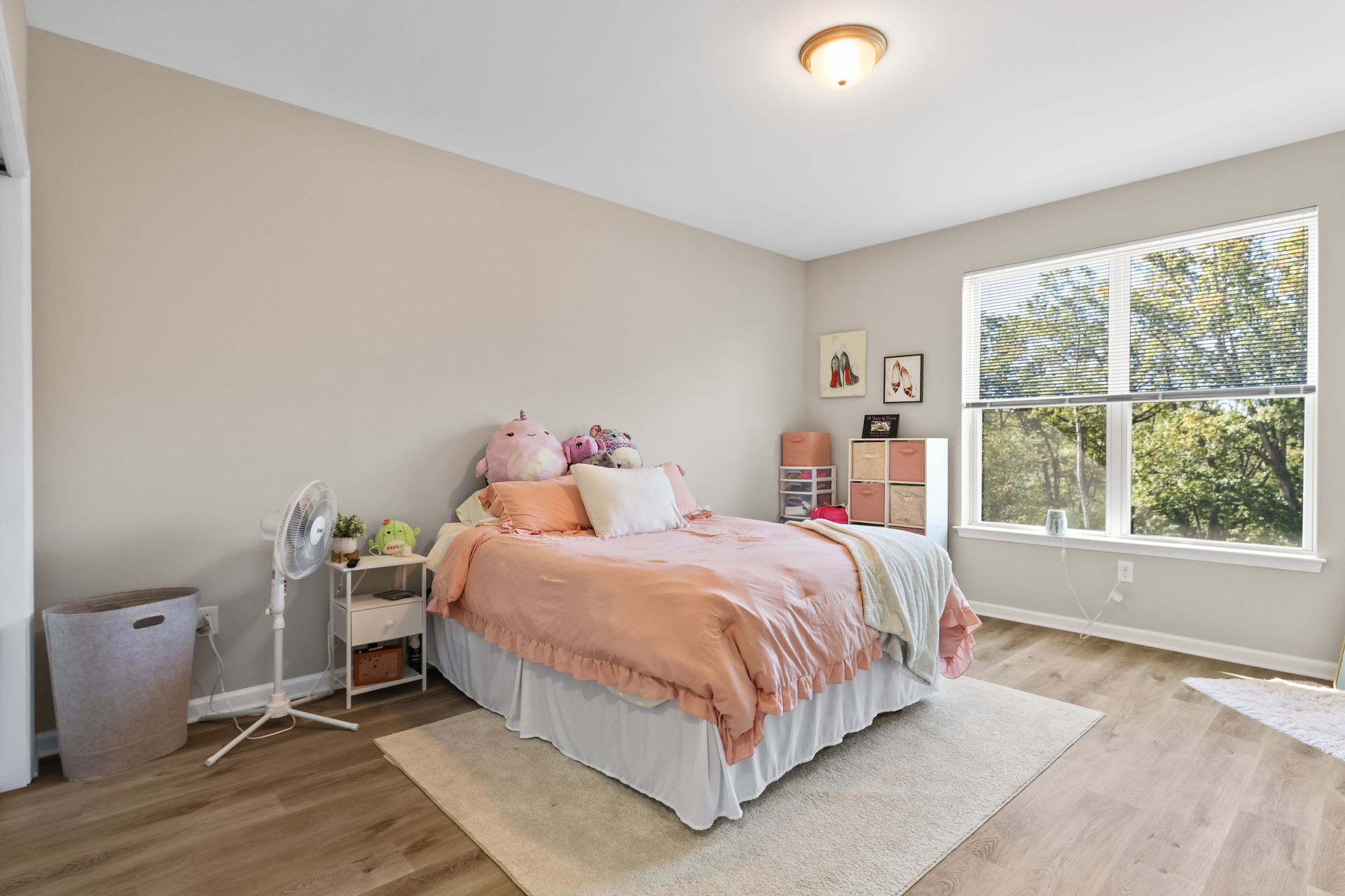 Bedroom with peach bedding, rug, window, and a standing fan.