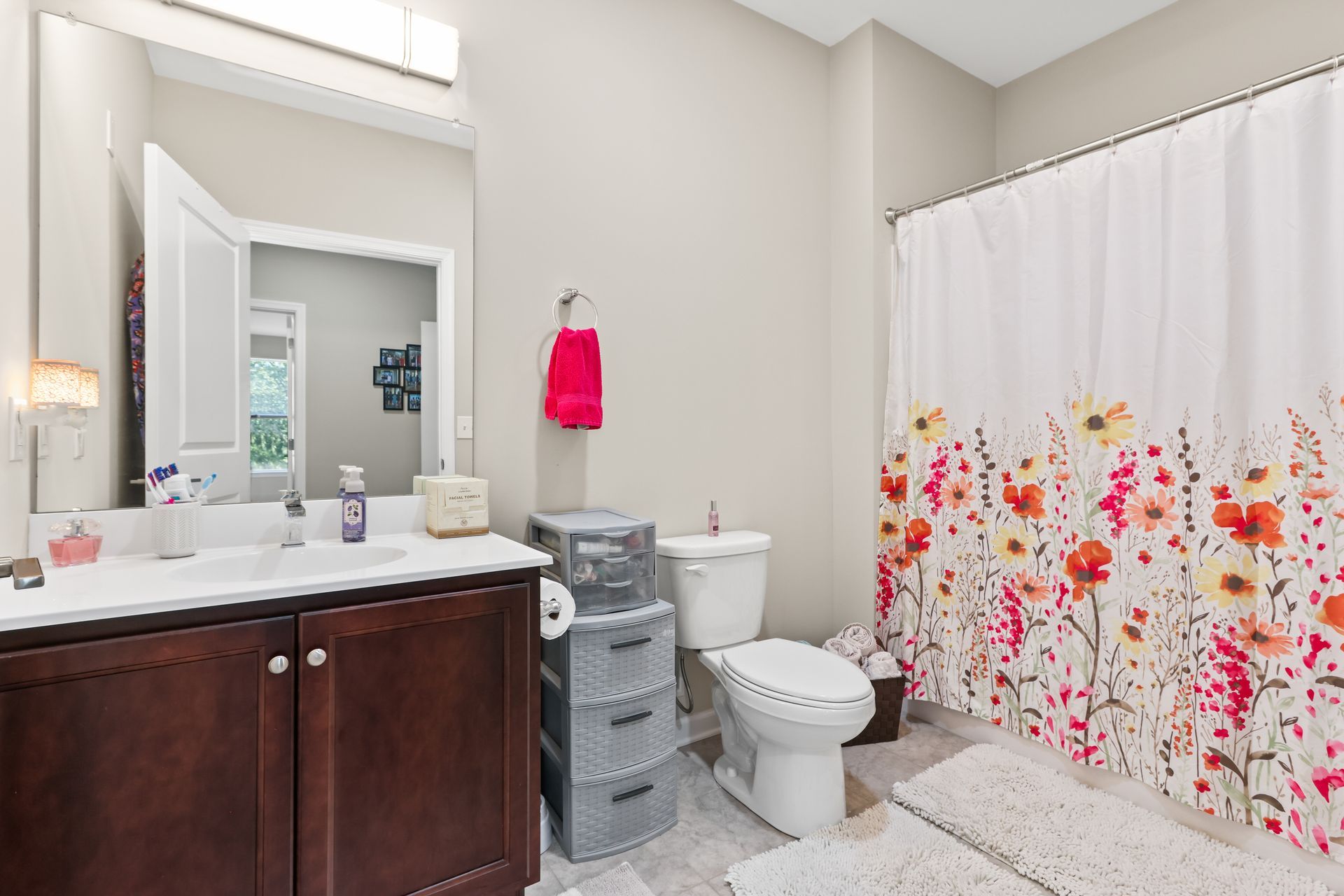 Bathroom with white walls, dark vanity, floral shower curtain, and a pink towel.