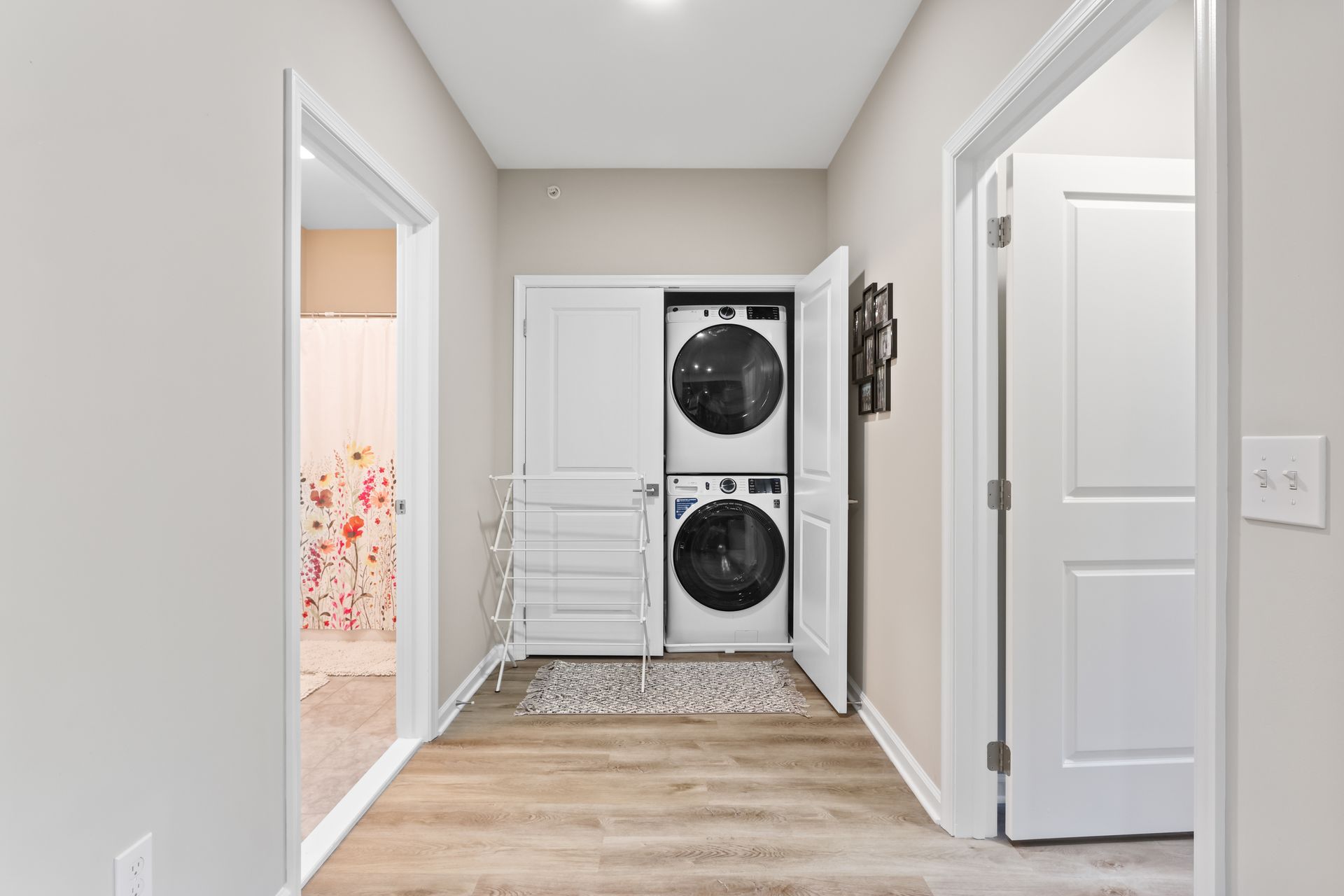 Hallway with stacked washer/dryer, doors on either side, light wood floor.
