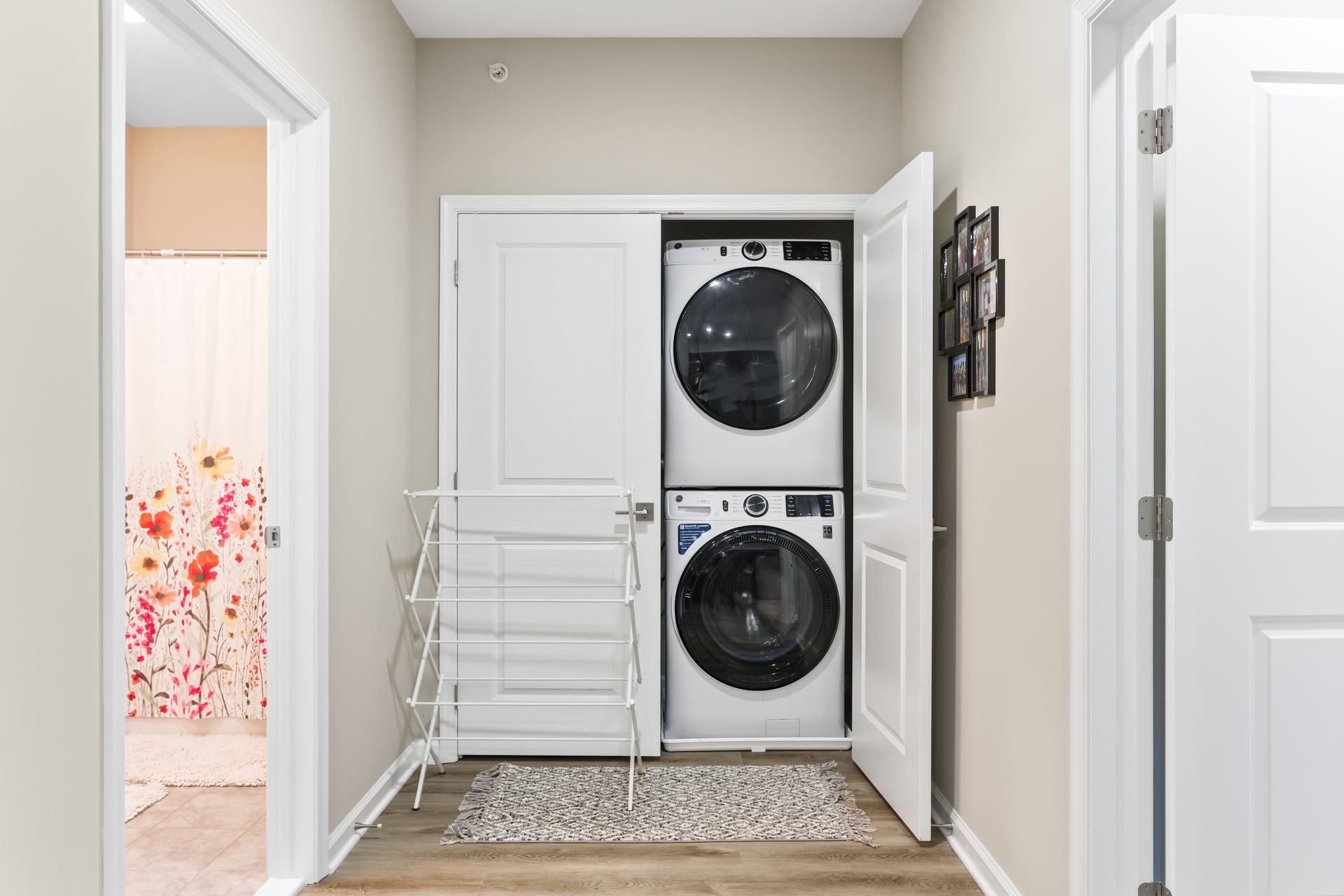 Laundry closet with stacked washer/dryer, drying rack, and bathroom doorway.