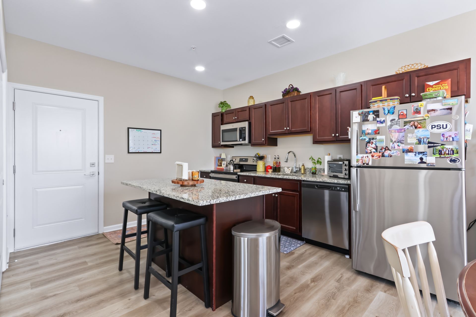 Kitchen with dark cabinets, stainless steel appliances, and a granite island with two stools.