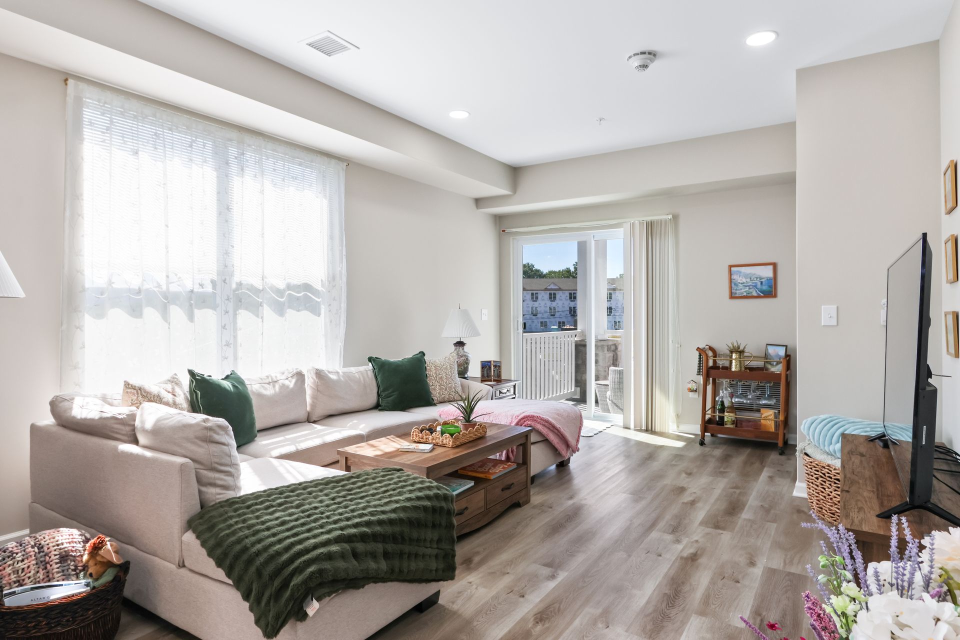 Cozy living room with sectional sofa, window, and balcony access. Beige and green colors dominate.
